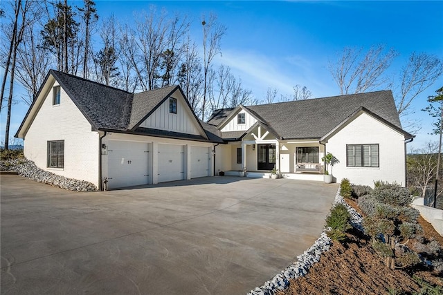 modern farmhouse with brick siding, roof with shingles, an attached garage, board and batten siding, and driveway