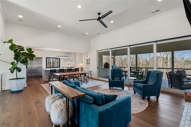 living room with a towering ceiling, visible vents, ornamental molding, and dark wood-style flooring