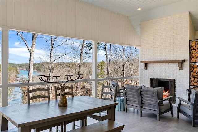 sunroom / solarium featuring an outdoor brick fireplace, lofted ceiling, and a water view