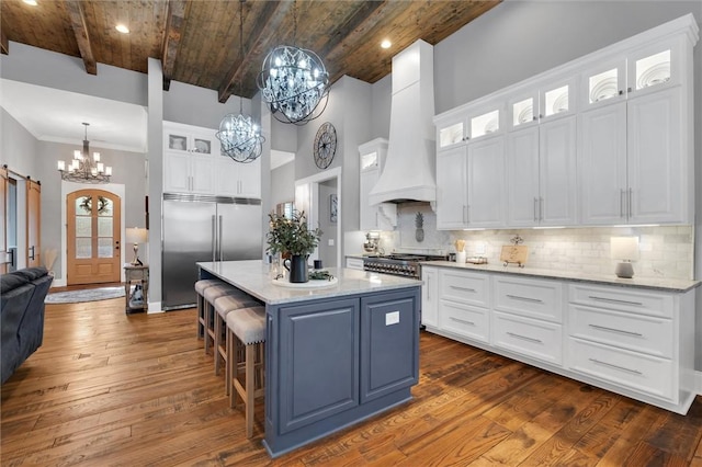 kitchen featuring dark wood-style floors, custom exhaust hood, an inviting chandelier, a barn door, and stainless steel built in fridge