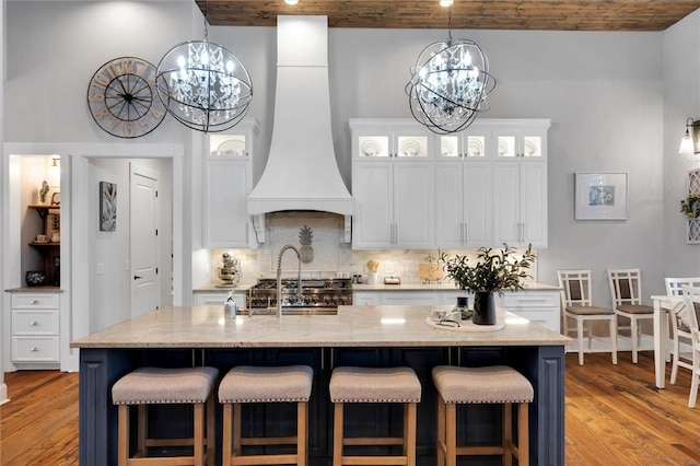 kitchen featuring light wood finished floors, custom range hood, light stone countertops, a high ceiling, and a chandelier