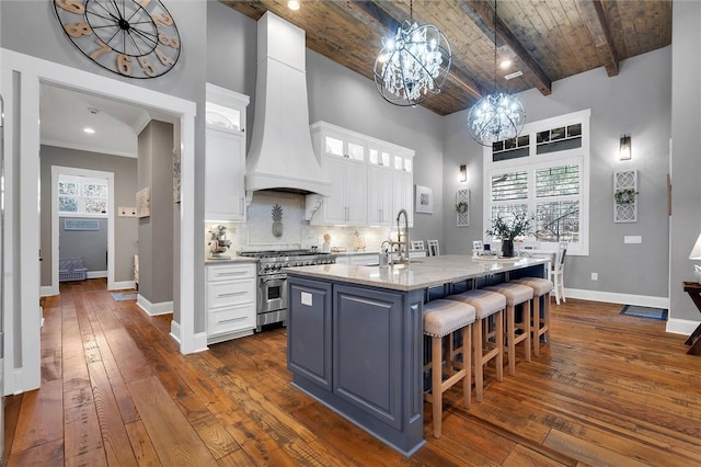 kitchen with stainless steel stove, premium range hood, a sink, wood ceiling, and white cabinetry