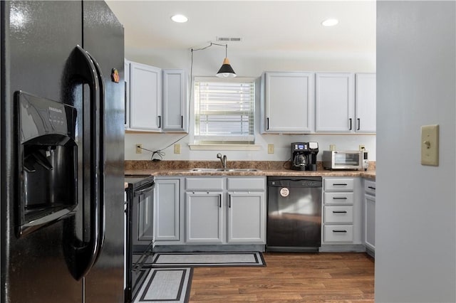 kitchen with recessed lighting, dark wood-type flooring, a sink, visible vents, and black appliances