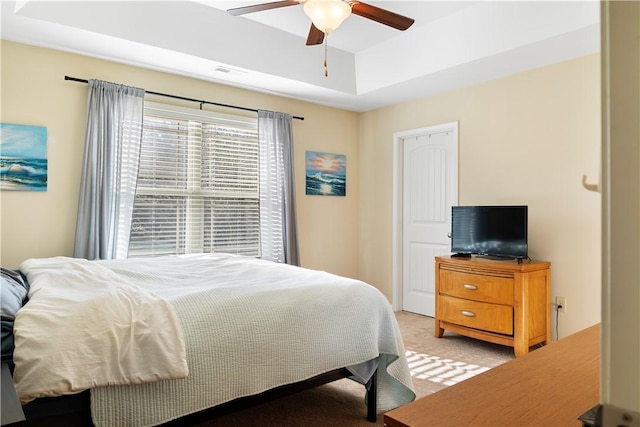 bedroom with a ceiling fan, visible vents, a tray ceiling, and light colored carpet