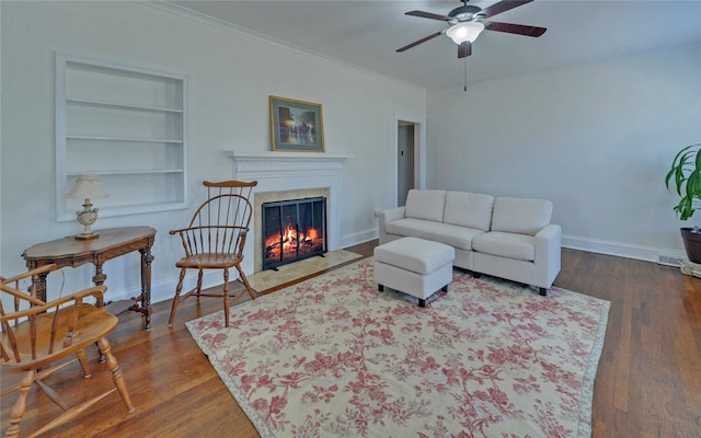 living area featuring baseboards, built in features, ornamental molding, wood finished floors, and a high end fireplace