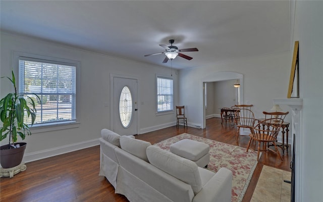 living room with arched walkways, crown molding, a ceiling fan, wood finished floors, and baseboards