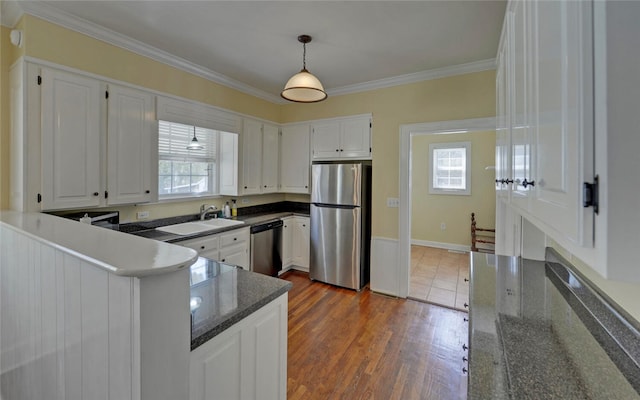 kitchen with white cabinets, ornamental molding, a sink, stainless steel appliances, and a wealth of natural light