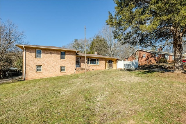 rear view of house with a chimney, fence, a lawn, and brick siding