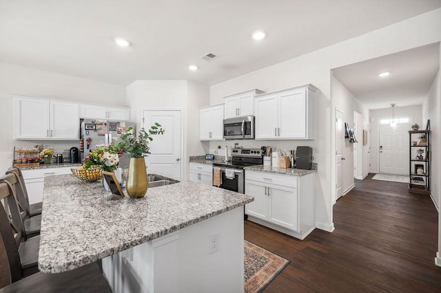 kitchen with light stone counters, dark wood-style floors, stainless steel appliances, an island with sink, and a kitchen breakfast bar