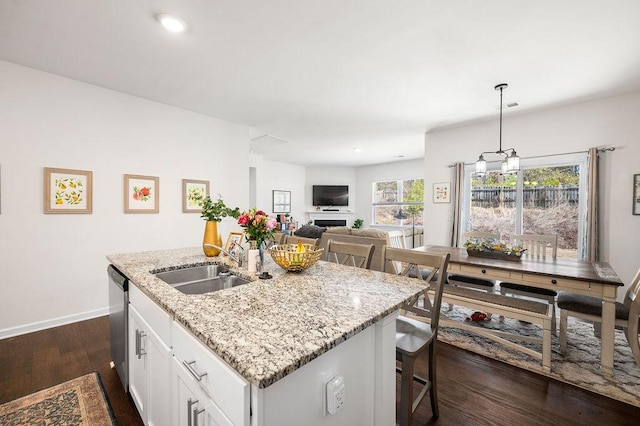 kitchen with dark wood finished floors, an island with sink, a fireplace, white cabinetry, and a sink