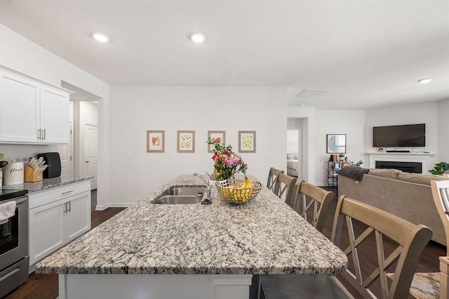 kitchen featuring a center island with sink, electric range, white cabinetry, a sink, and light stone countertops