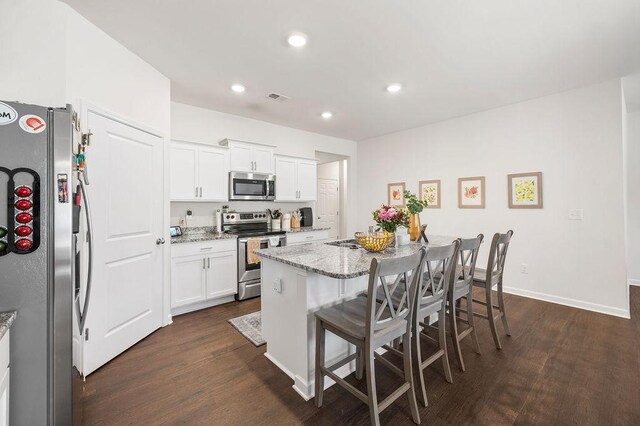 kitchen featuring dark wood finished floors, a breakfast bar area, stainless steel appliances, visible vents, and light stone countertops