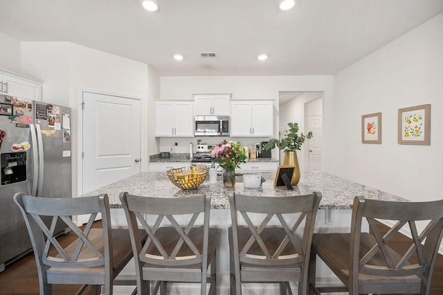 kitchen with recessed lighting, white cabinetry, a kitchen breakfast bar, appliances with stainless steel finishes, and light stone countertops