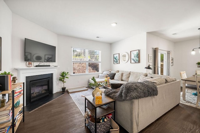 living room featuring dark wood-type flooring, a glass covered fireplace, visible vents, and baseboards