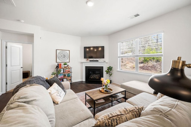 living area featuring baseboards, visible vents, dark wood finished floors, and a glass covered fireplace