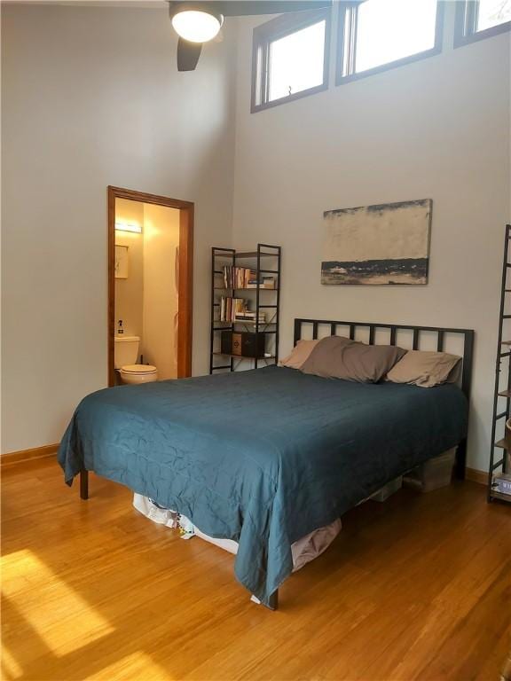 bedroom with ensuite bathroom, a towering ceiling, baseboards, and wood finished floors