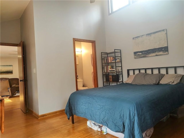 bedroom with ensuite bath, a high ceiling, baseboards, and wood finished floors