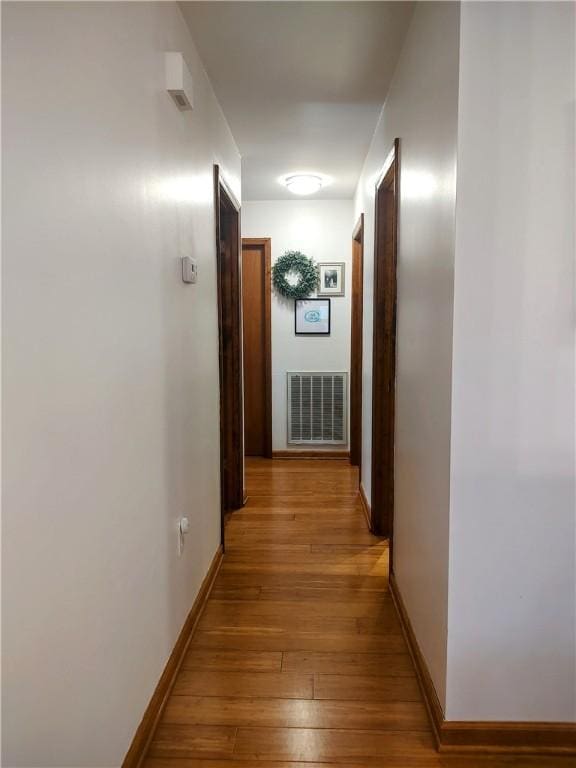 hallway with light wood-type flooring, visible vents, and baseboards