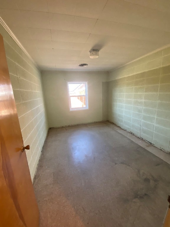 empty room featuring concrete block wall, visible vents, and concrete floors