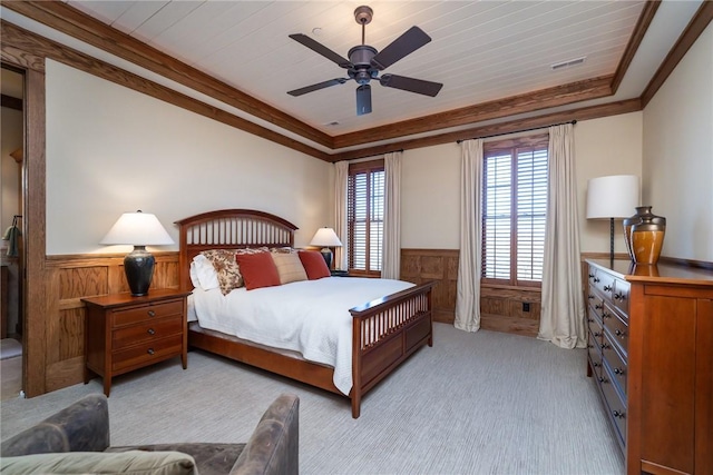 bedroom with a wainscoted wall, crown molding, a raised ceiling, visible vents, and light carpet