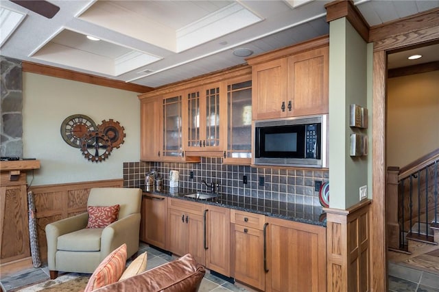 kitchen featuring wainscoting, glass insert cabinets, a sink, black microwave, and backsplash