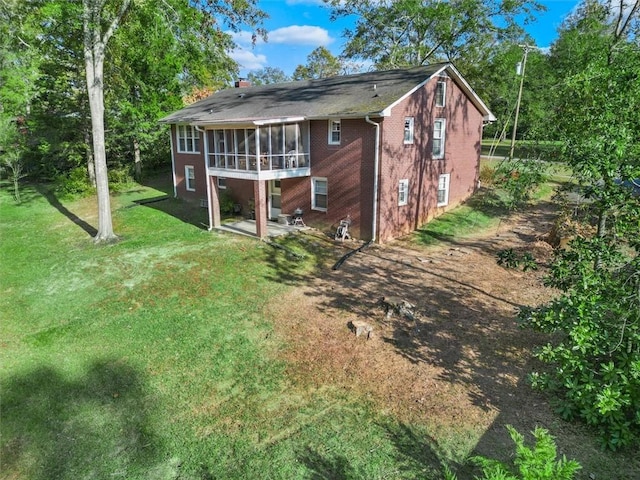 rear view of property with a sunroom, a yard, a chimney, and brick siding