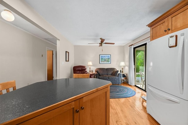 kitchen with brown cabinets, dark countertops, a ceiling fan, freestanding refrigerator, and light wood-type flooring