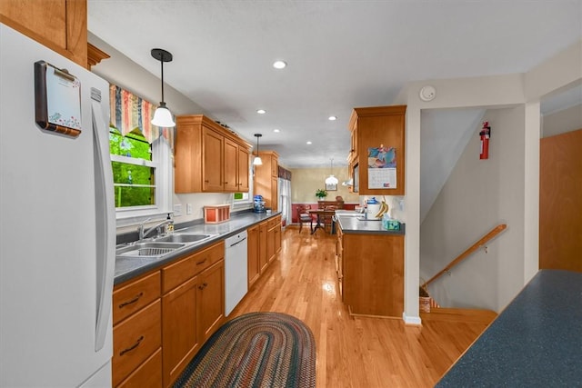 kitchen featuring dark countertops, hanging light fixtures, light wood-style floors, a sink, and white appliances