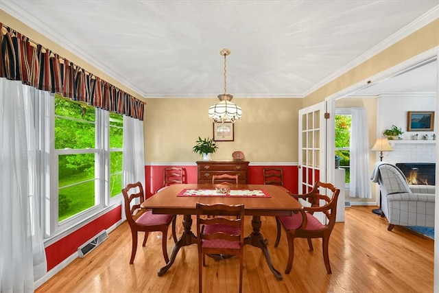 dining area with crown molding, a brick fireplace, visible vents, and light wood-style floors