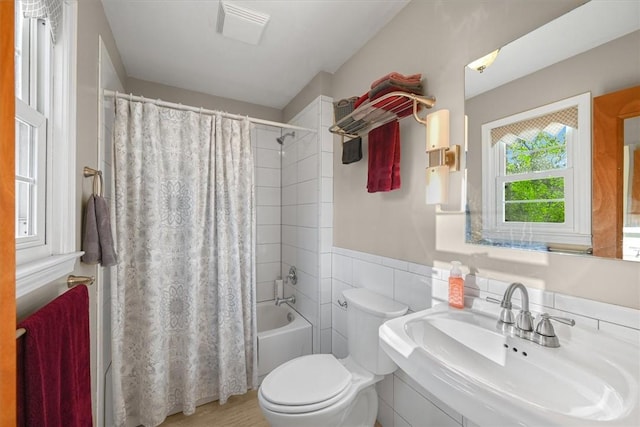 full bath featuring toilet, a wainscoted wall, a sink, shower / bath combo with shower curtain, and tile walls