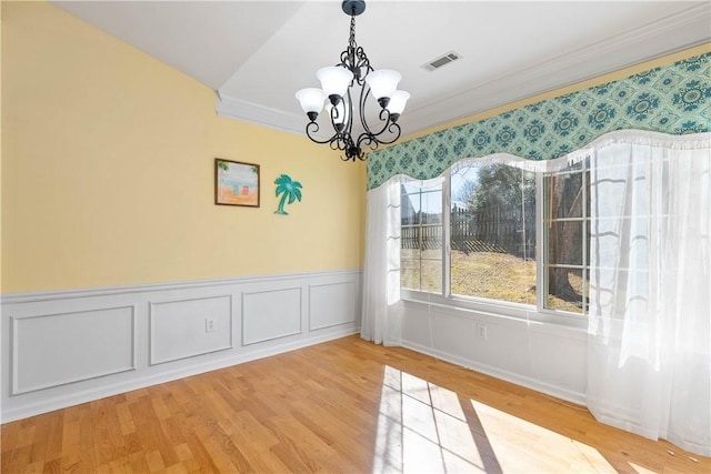 unfurnished dining area featuring visible vents, a wainscoted wall, ornamental molding, wood finished floors, and a chandelier