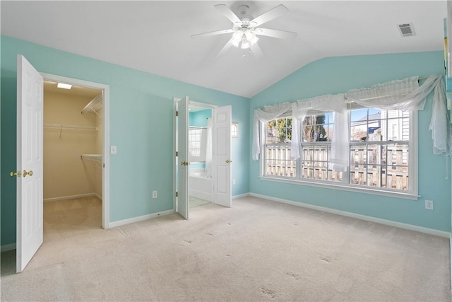 unfurnished bedroom featuring a walk in closet, carpet, lofted ceiling, visible vents, and baseboards