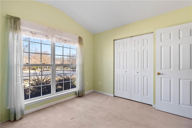 unfurnished bedroom featuring carpet floors, a closet, vaulted ceiling, and baseboards