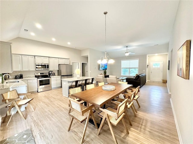 dining space featuring vaulted ceiling, ceiling fan with notable chandelier, light wood-type flooring, and baseboards