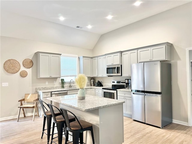 kitchen featuring light stone counters, a center island, a breakfast bar, appliances with stainless steel finishes, and a sink