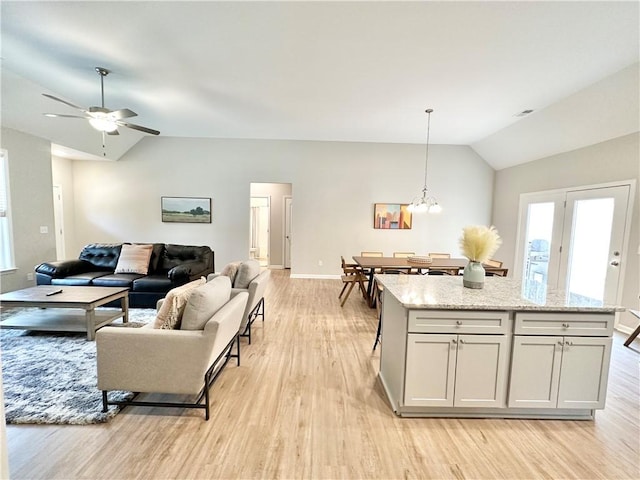 living area featuring lofted ceiling, light wood-style flooring, a wealth of natural light, and ceiling fan with notable chandelier