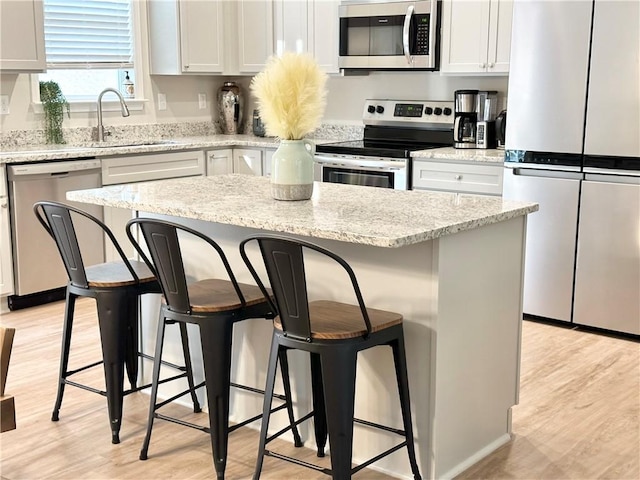 kitchen with stainless steel appliances, light wood finished floors, a sink, and a kitchen breakfast bar