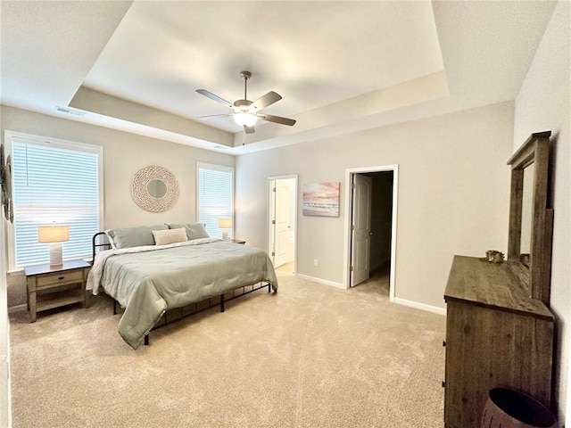 bedroom featuring light carpet, a ceiling fan, visible vents, baseboards, and a tray ceiling