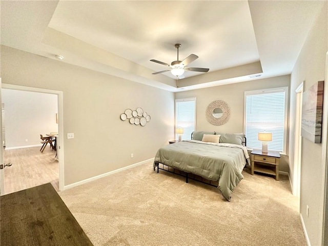 bedroom featuring multiple windows, baseboards, a raised ceiling, and light colored carpet