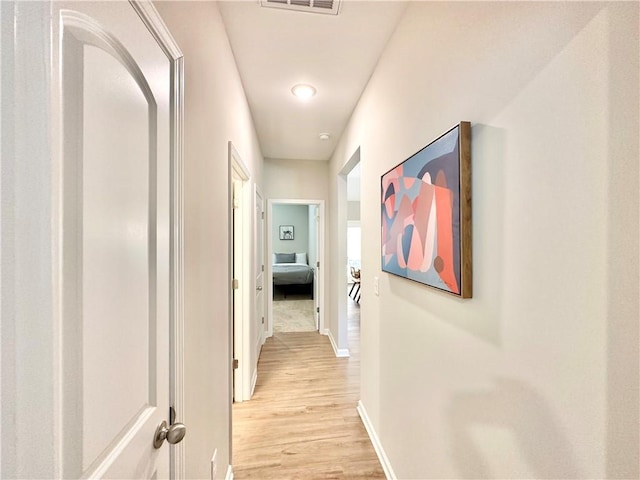 hallway featuring visible vents, light wood-style flooring, and baseboards