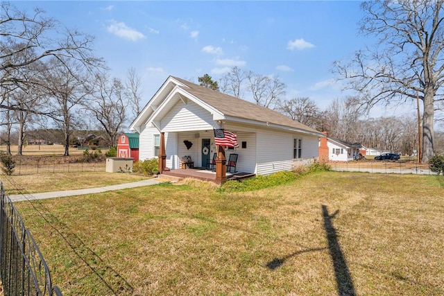 bungalow with an outbuilding, covered porch, a storage shed, fence, and a front lawn