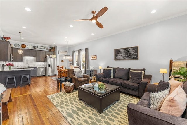 living room with recessed lighting, wood-type flooring, ornamental molding, and ceiling fan with notable chandelier