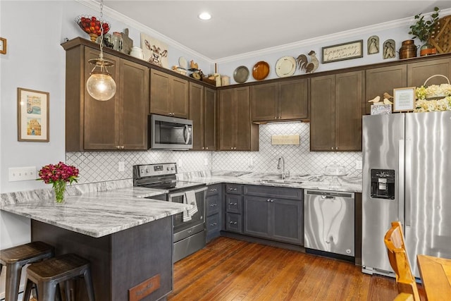 kitchen with appliances with stainless steel finishes, ornamental molding, a peninsula, dark brown cabinets, and a sink