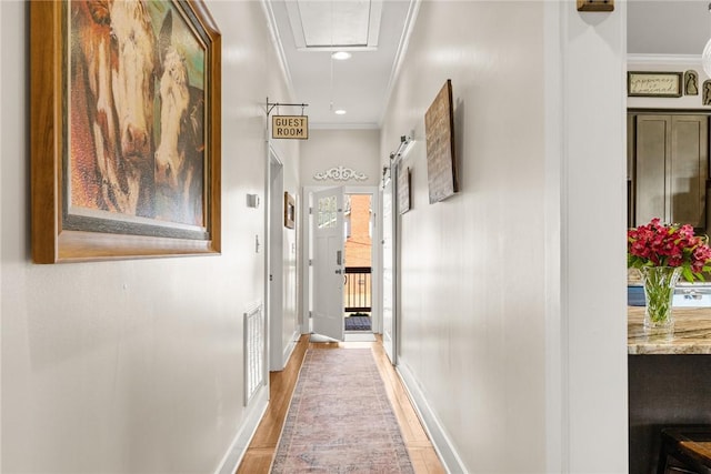 corridor featuring crown molding, visible vents, a barn door, attic access, and baseboards