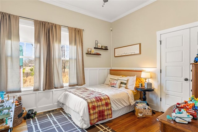 bedroom with a wainscoted wall, crown molding, a decorative wall, and wood finished floors