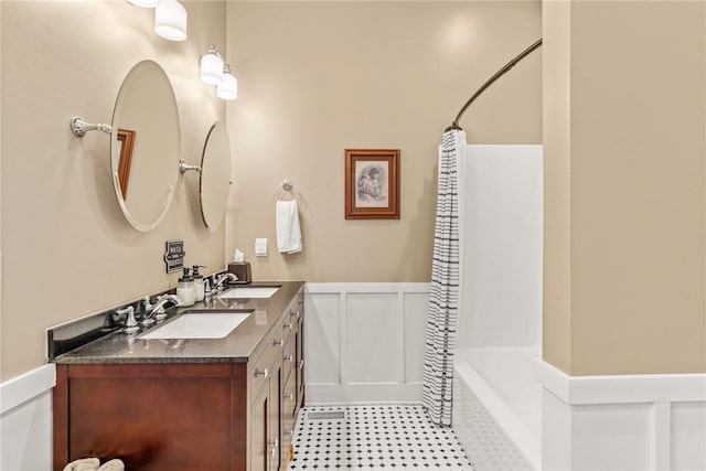 full bathroom featuring wainscoting, a sink, a decorative wall, and double vanity