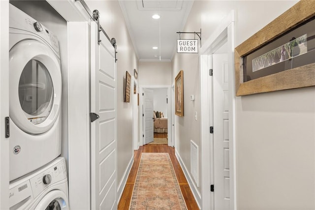 laundry room with laundry area, a barn door, attic access, crown molding, and stacked washing maching and dryer