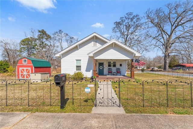 bungalow-style home with a fenced front yard, a storage unit, a porch, a front yard, and an outdoor structure