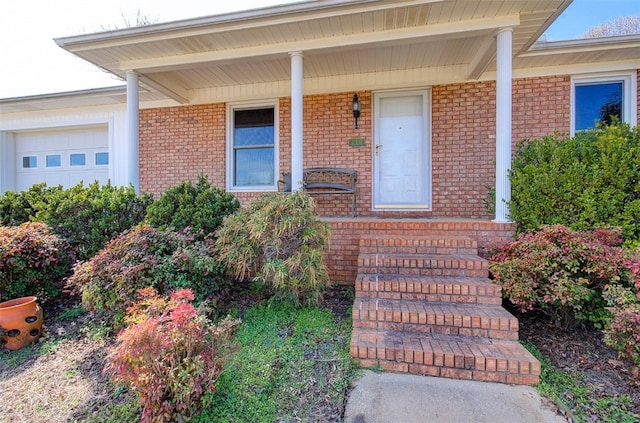 property entrance featuring a porch, brick siding, and an attached garage