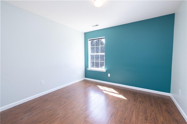 spare room with wood finished floors, visible vents, and baseboards